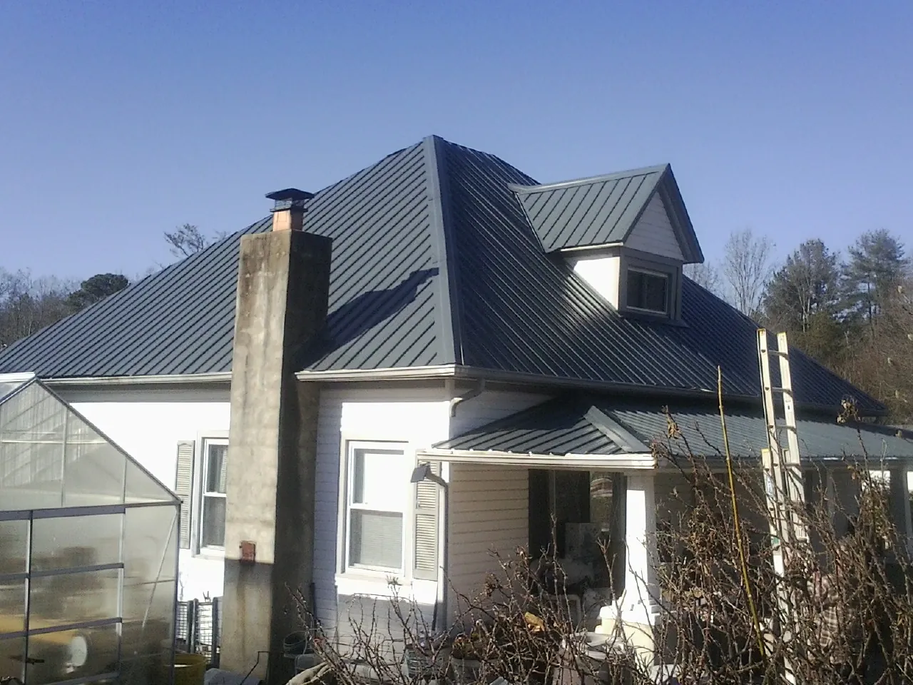 Dark blue standing seam metal roof on a white farmhouse with dormer — Slate & Tile Roof Repair by Roofing Brothers in Geneseo